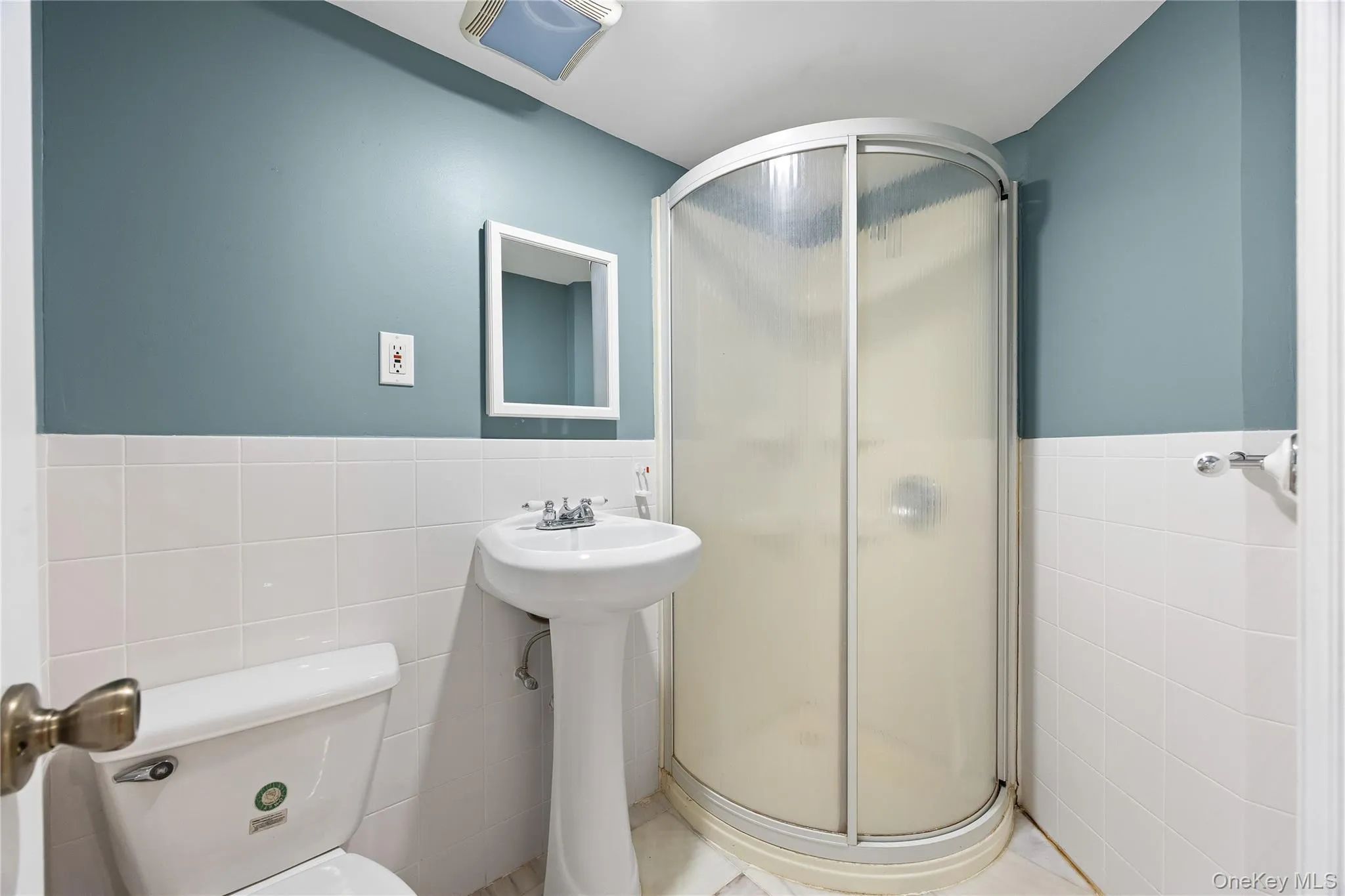 Full bath with tile walls, a stall shower, and a wainscoted wall Full bath with tile walls, a stall shower, and a wainscoted wall