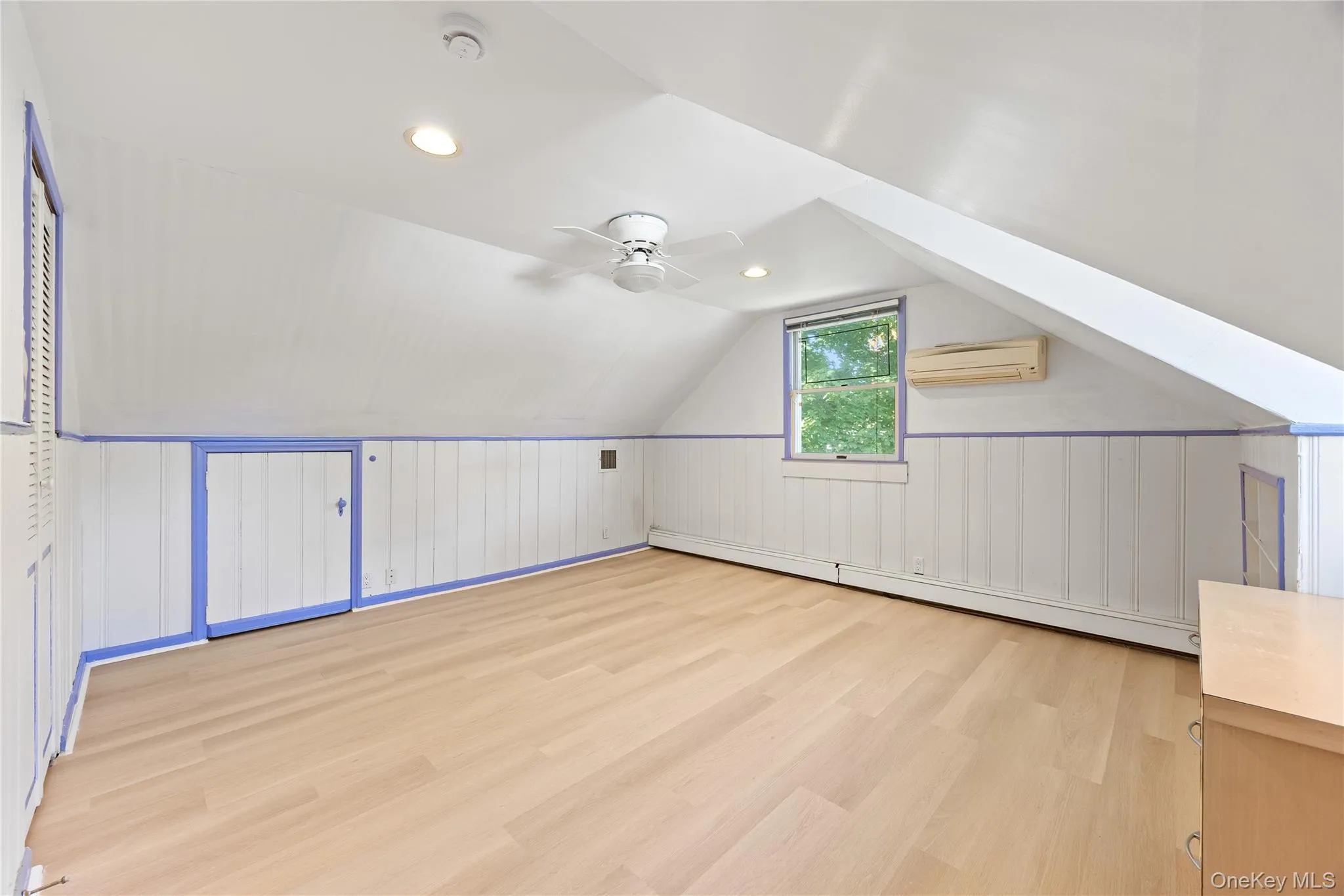 Additional living space featuring light wood-style flooring, vaulted ceiling, a baseboard radiator, an AC wall unit, and recessed lighting Additional living space featuring light wood-style flooring, vaulted ceiling, a baseboard radiator, an AC wall unit, and recessed lighting