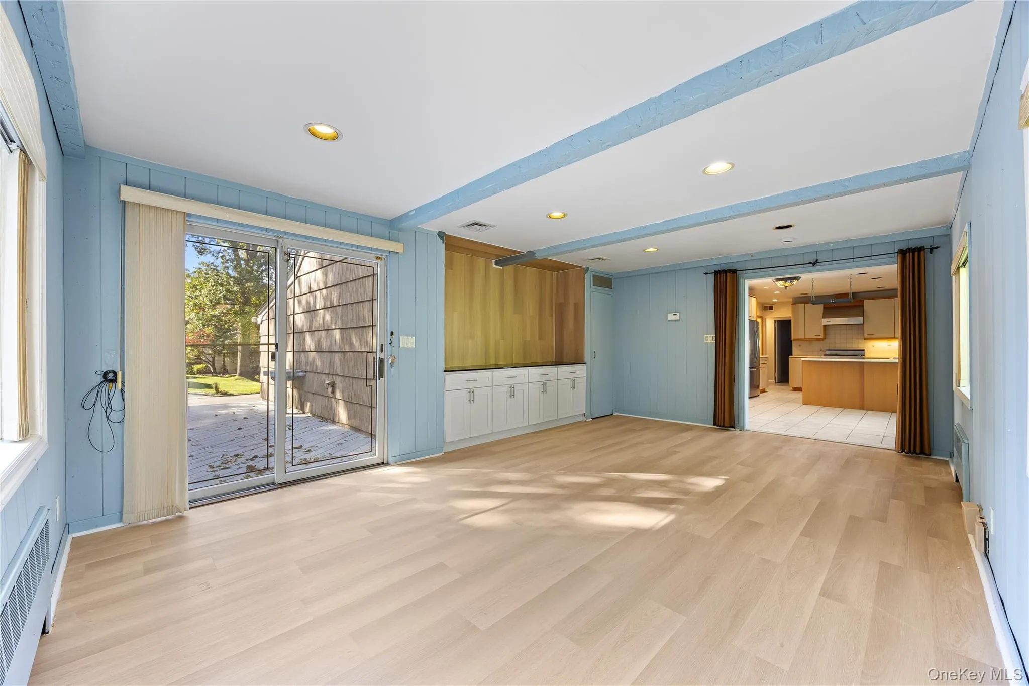 Unfurnished living room featuring light wood finished floors, wooden walls, radiator, and recessed lighting Unfurnished living room featuring light wood finished floors, wooden walls, radiator, and recessed lighting