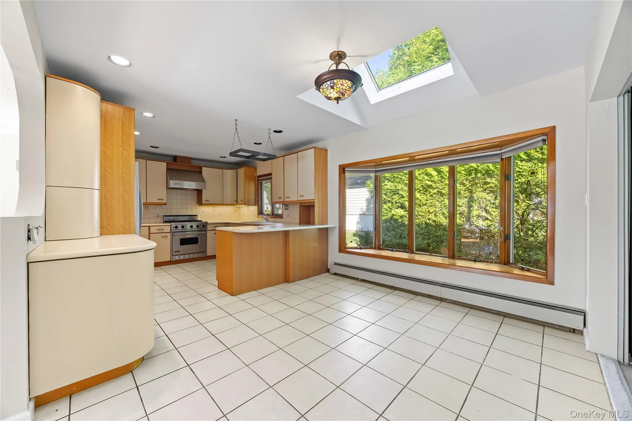Kitchen featuring a skylight, a baseboard radiator, light countertops, water heater, and tasteful backsplash Kitchen featuring a skylight, a baseboard radiator, light countertops, water heater, and tasteful backsplash