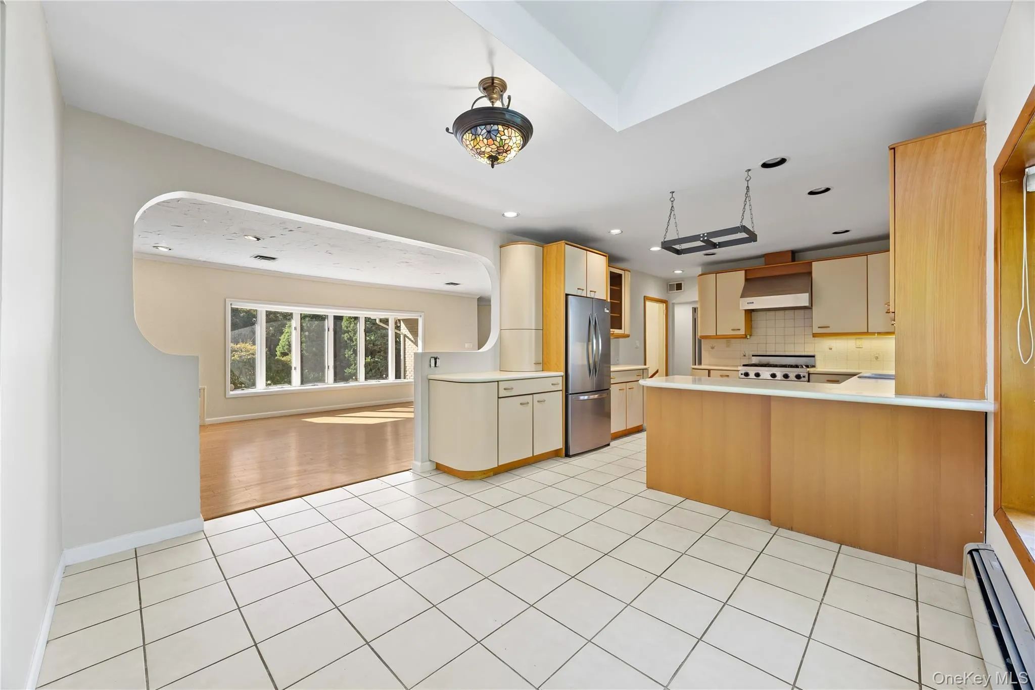 Kitchen featuring a peninsula, backsplash, a baseboard heating unit, light tile patterned flooring, and light countertops Kitchen featuring a peninsula, backsplash, a baseboard heating unit, light tile patterned flooring, and light countertops