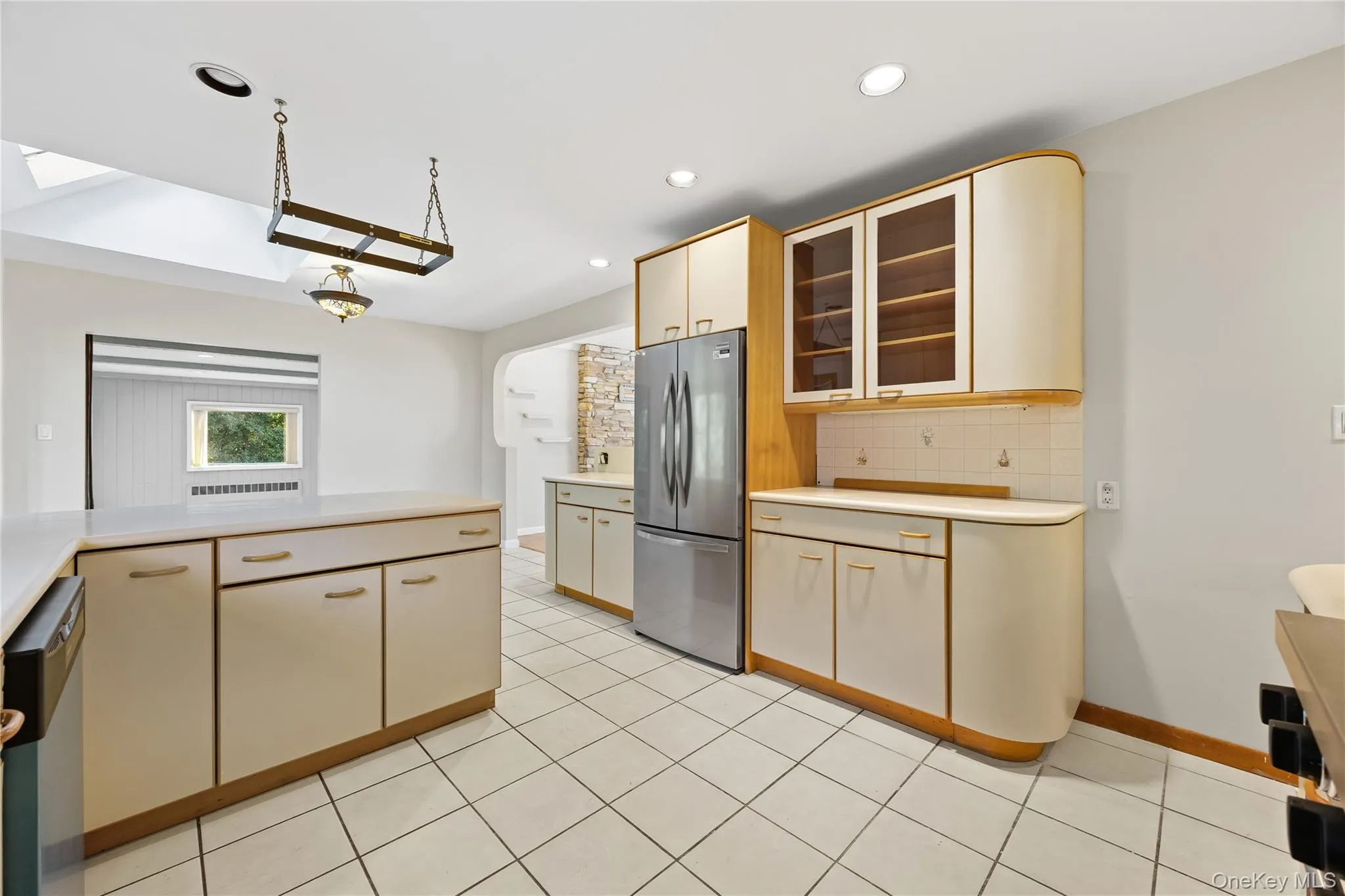 Kitchen with decorative backsplash, light countertops, glass insert cabinets, appliances with stainless steel finishes, and light tile patterned floors Kitchen with decorative backsplash, light countertops, glass insert cabinets, appliances with stainless steel finishes, and light tile patterned floors