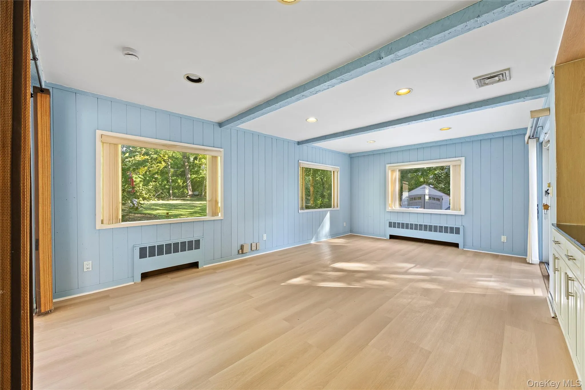 Unfurnished living room featuring radiator heating unit, light wood-style floors, beamed ceiling, recessed lighting, and wood walls Unfurnished living room featuring radiator heating unit, light wood-style floors, beamed ceiling, recessed lighting, and wood walls