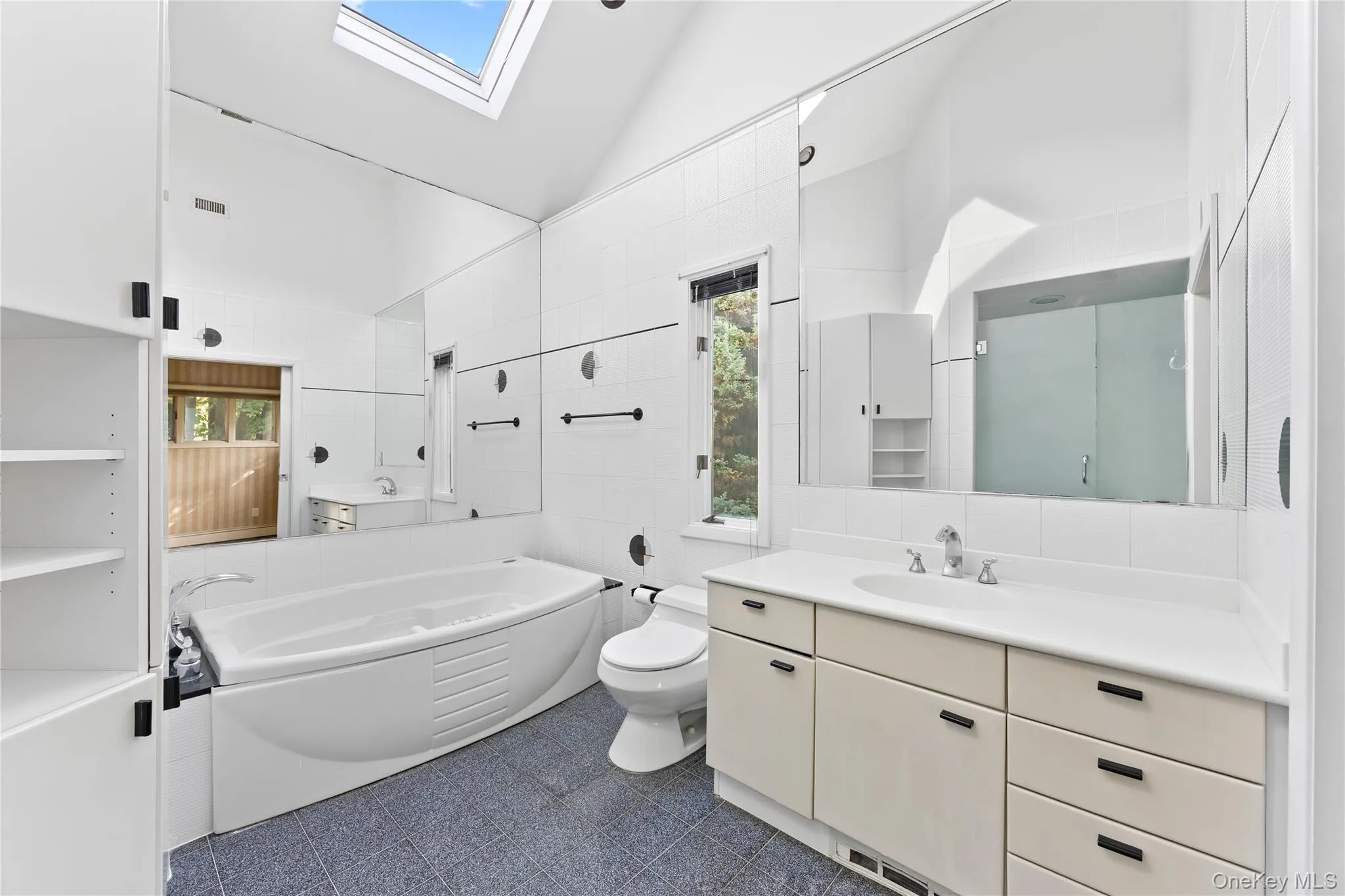 Full bathroom featuring a skylight, a bath, vanity, tile walls, and high vaulted ceiling Full bathroom featuring a skylight, a bath, vanity, tile walls, and high vaulted ceiling
