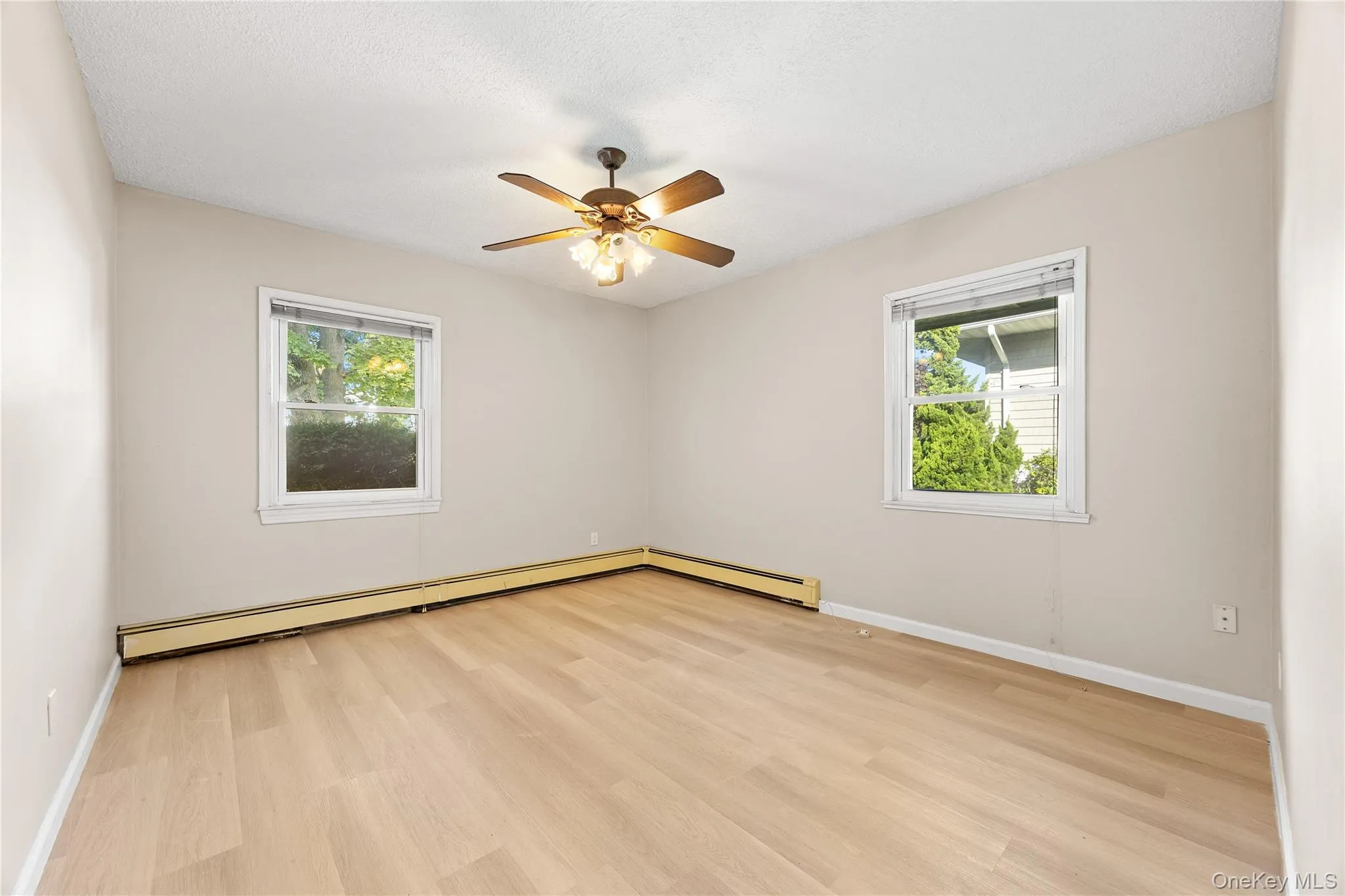 Empty room featuring healthy amount of natural light, light wood-type flooring, and a baseboard heating unit Empty room featuring healthy amount of natural light, light wood-type flooring, and a baseboard heating unit
