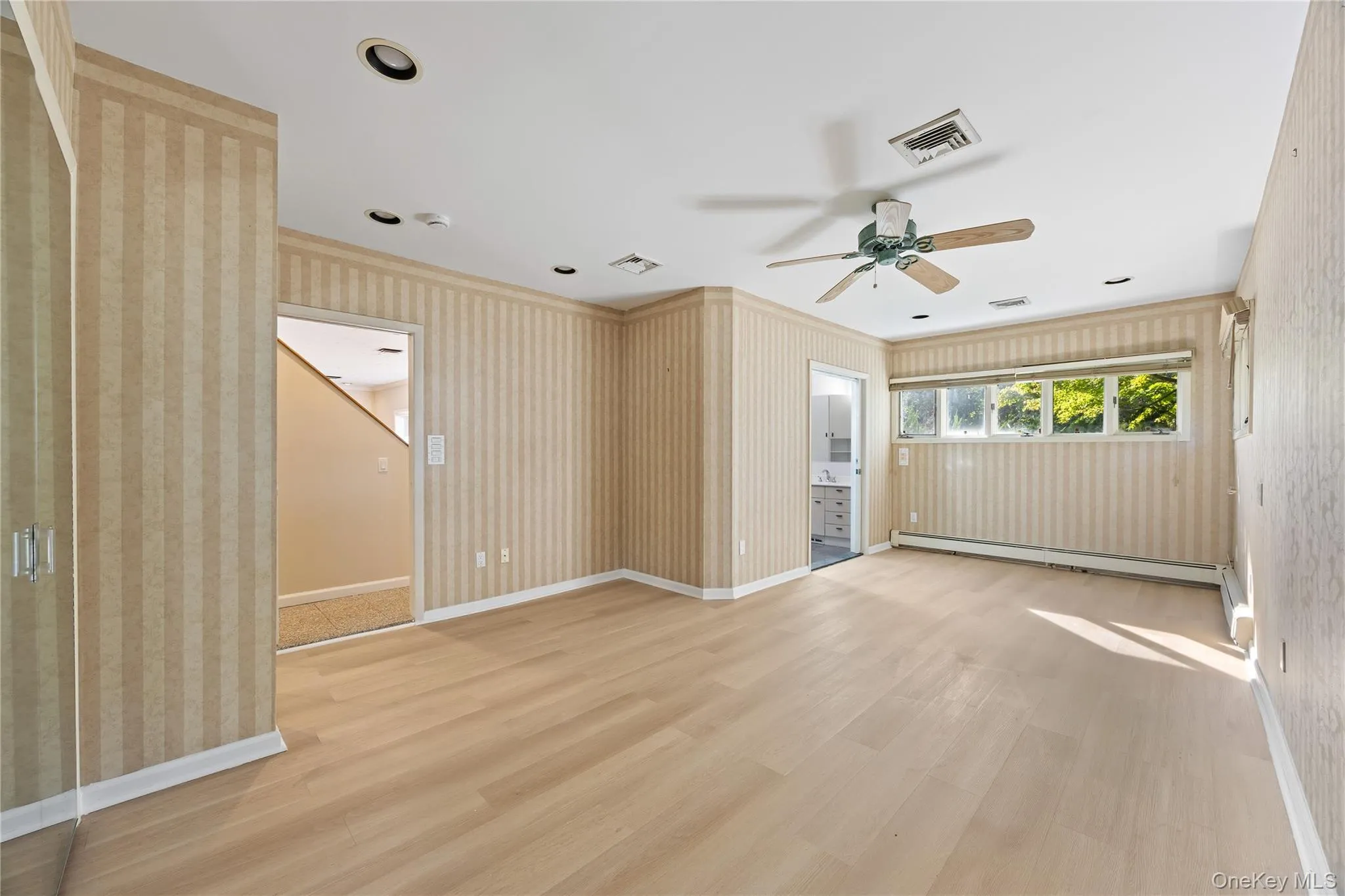Spare room featuring ornamental molding, a ceiling fan, wallpapered walls, light wood-style floors, and baseboard heating Spare room featuring ornamental molding, a ceiling fan, wallpapered walls, light wood-style floors, and baseboard heating