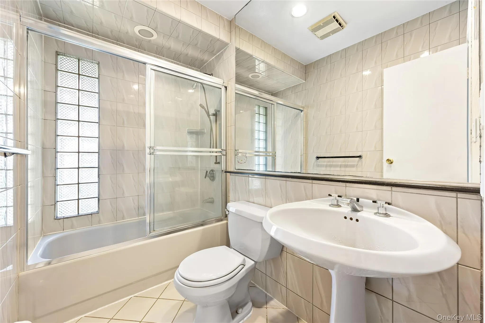 Full bathroom featuring tile walls, combined bath / shower with glass door, and tile patterned flooring Full bathroom featuring tile walls, combined bath / shower with glass door, and tile patterned flooring