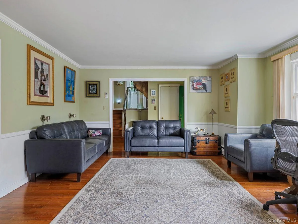 Living room with a wainscoted wall, ornamental molding, wood finished floors, and healthy amount of natural light Living room with a wainscoted wall, ornamental molding, wood finished floors, and healthy amount of natural light