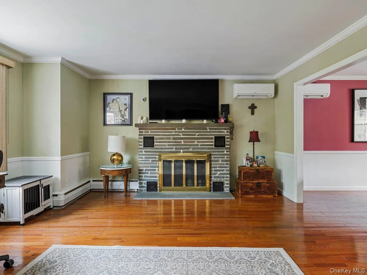 Living area featuring crown molding, a glass covered fireplace, light wood-style floors, a wall unit AC, and a baseboard radiator Living area featuring crown molding, a glass covered fireplace, light wood-style floors, a wall unit AC, and a baseboard radiator