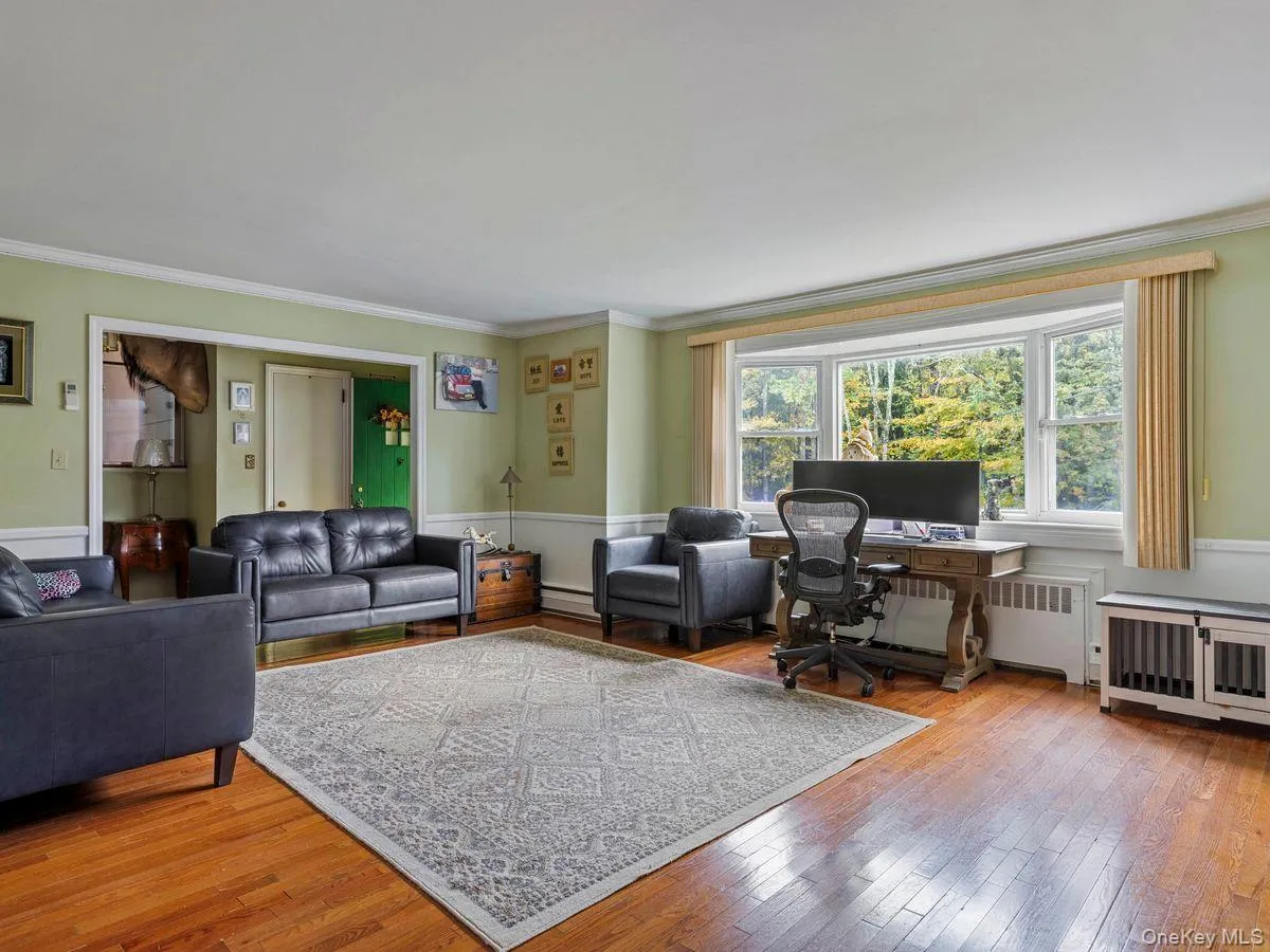 Living area with ornamental molding, hardwood / wood-style flooring, radiator heating unit, an office area, and baseboard heating Living area with ornamental molding, hardwood / wood-style flooring, radiator heating unit, an office area, and baseboard heating