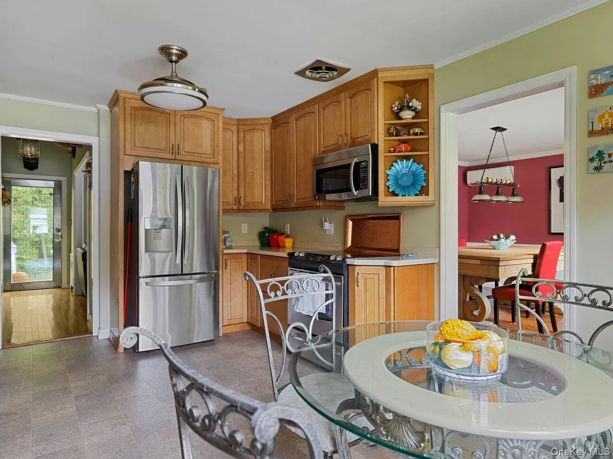 Kitchen with crown molding, stainless steel appliances, light countertops, open shelves, and brown cabinetry Kitchen with crown molding, stainless steel appliances, light countertops, open shelves, and brown cabinetry