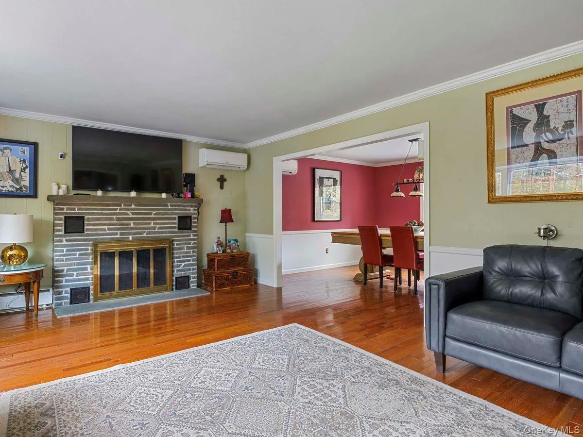 Living room featuring wood finished floors, crown molding, a glass covered fireplace, a wall unit AC, and a baseboard heating unit Living room featuring wood finished floors, crown molding, a glass covered fireplace, a wall unit AC, and a baseboard heating unit