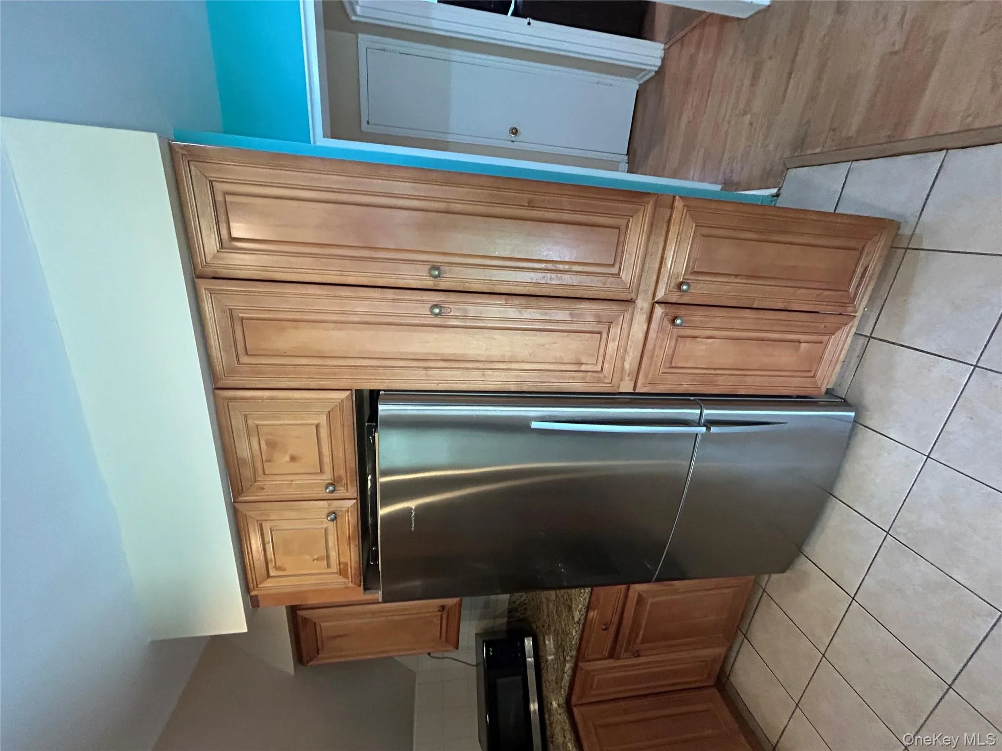 Kitchen with stainless steel fridge, brown cabinetry, dark stone counters, and light tile patterned floors Kitchen with stainless steel fridge, brown cabinetry, dark stone counters, and light tile patterned floors
