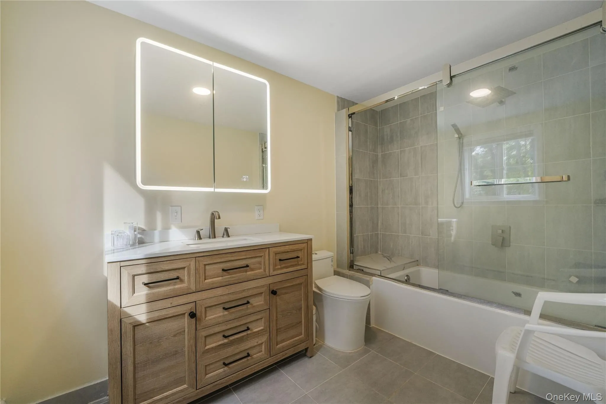 Bathroom with shower / bath combination with glass door, vanity, and light tile patterned floors Bathroom with shower / bath combination with glass door, vanity, and light tile patterned floors