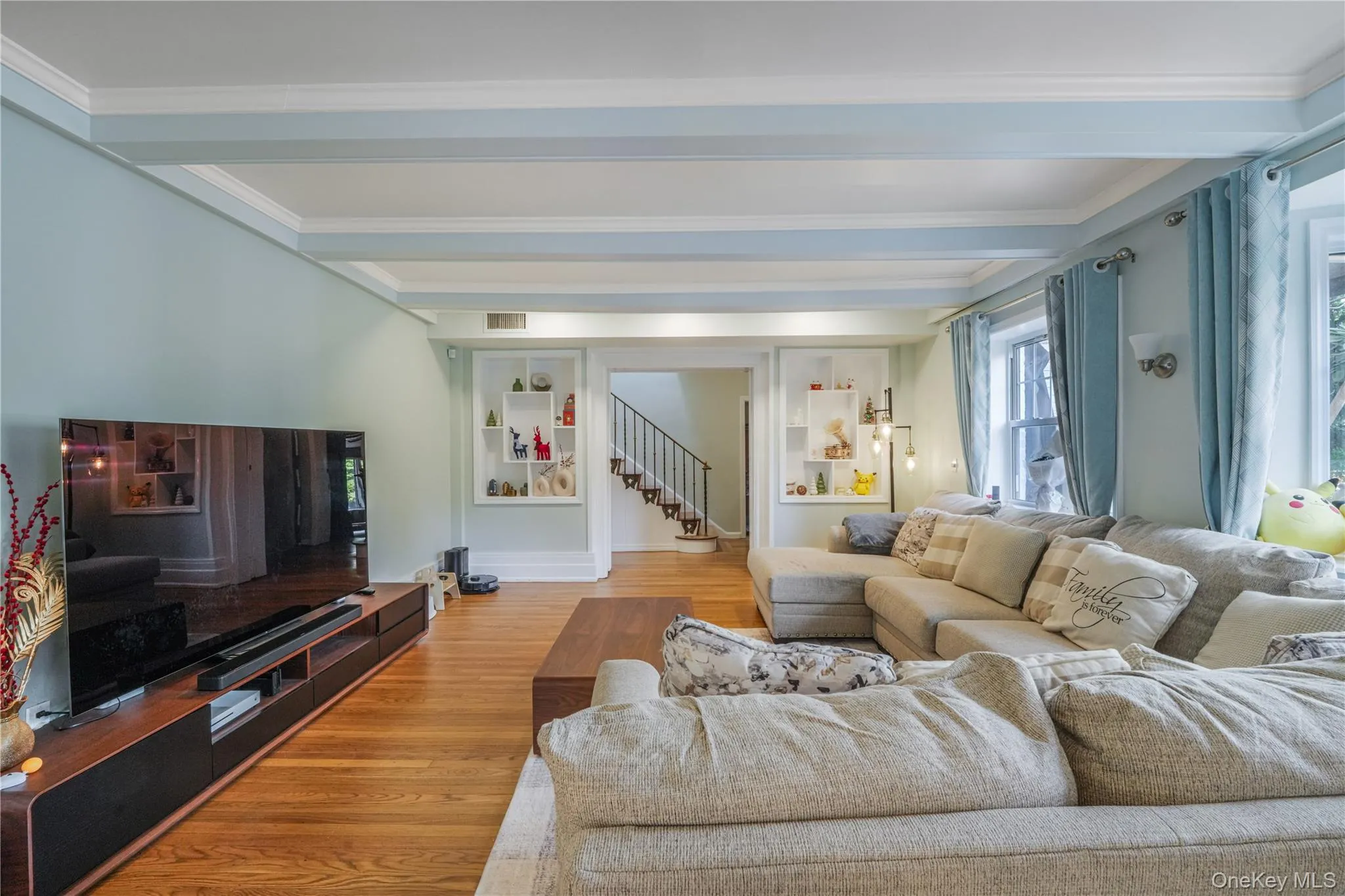 Living room featuring beam ceiling, wood finished floors, stairs, and crown molding Living room featuring beam ceiling, wood finished floors, stairs, and crown molding