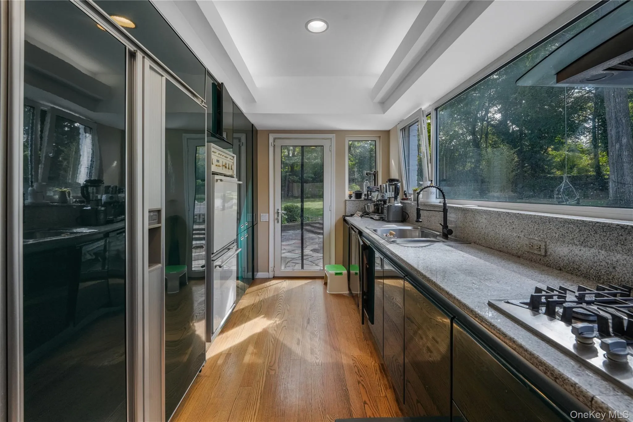 Kitchen with high end fridge, a tray ceiling, light wood-style flooring, stainless steel gas stovetop, and extractor fan Kitchen with high end fridge, a tray ceiling, light wood-style flooring, stainless steel gas stovetop, and extractor fan