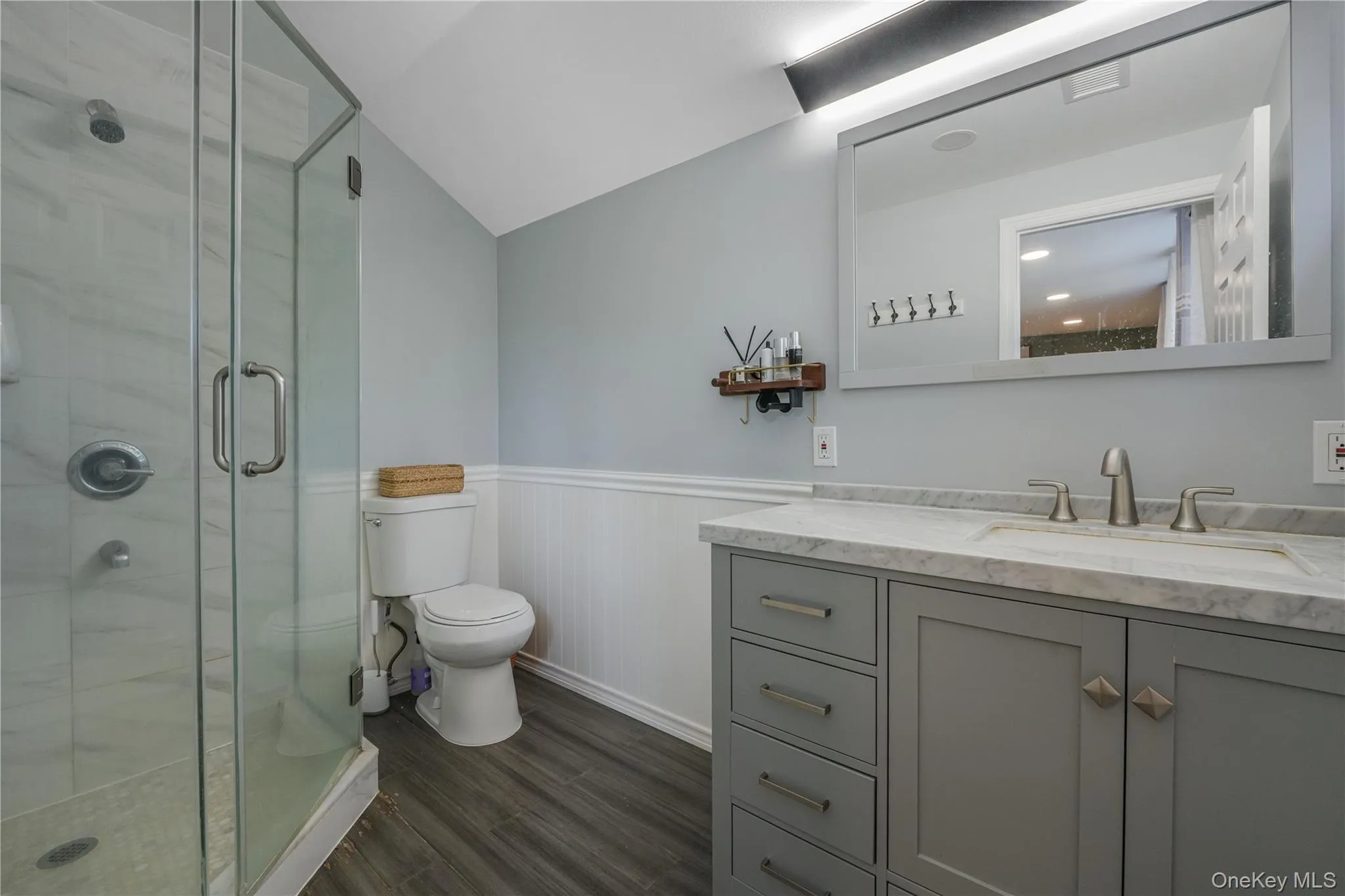 Full bathroom with a wainscoted wall, dark wood-type flooring, vanity, a stall shower, and vaulted ceiling Full bathroom with a wainscoted wall, dark wood-type flooring, vanity, a stall shower, and vaulted ceiling