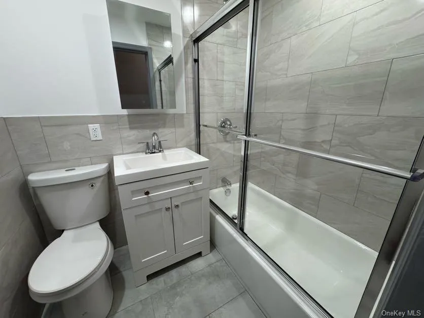 Bathroom with vanity, bath / shower combo with glass door, and tile walls Bathroom with vanity, bath / shower combo with glass door, and tile walls
