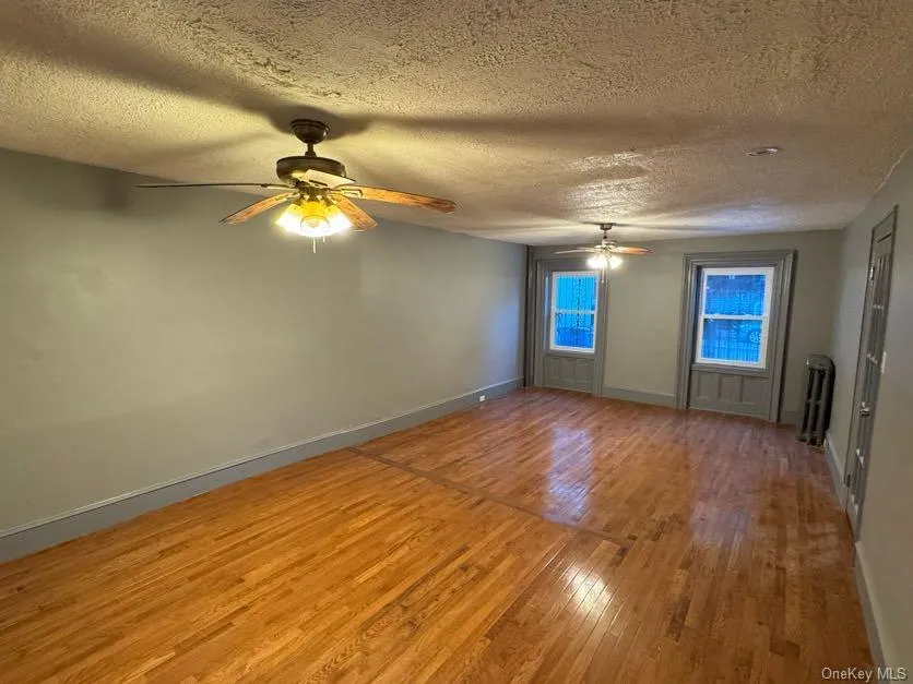 Spare room featuring a textured ceiling, light wood-style floors, ceiling fan, and radiator heating unit Spare room featuring a textured ceiling, light wood-style floors, ceiling fan, and radiator heating unit