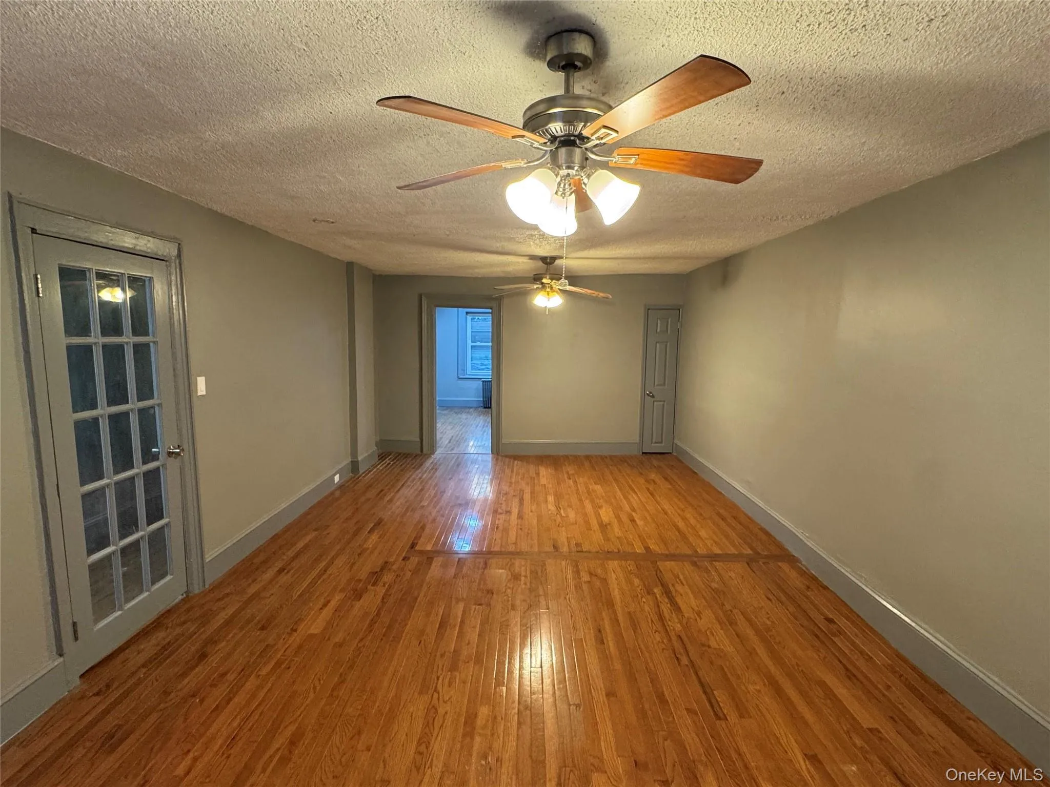 Empty room with wood-type flooring, a textured ceiling, and ceiling fan Empty room with wood-type flooring, a textured ceiling, and ceiling fan