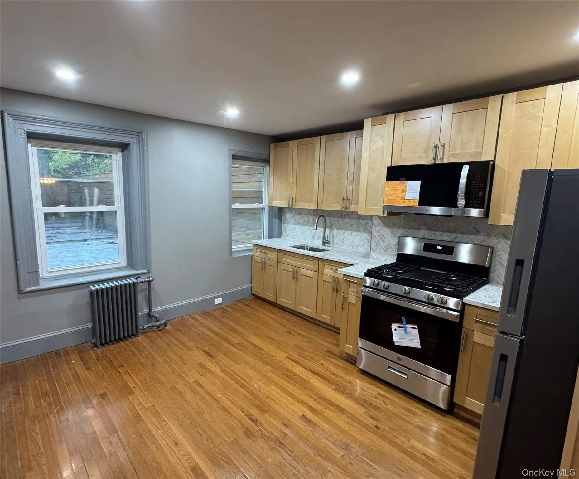 Kitchen featuring appliances with stainless steel finishes, tasteful backsplash, light wood finished floors, light stone counters, and radiator Kitchen featuring appliances with stainless steel finishes, tasteful backsplash, light wood finished floors, light stone counters, and radiator