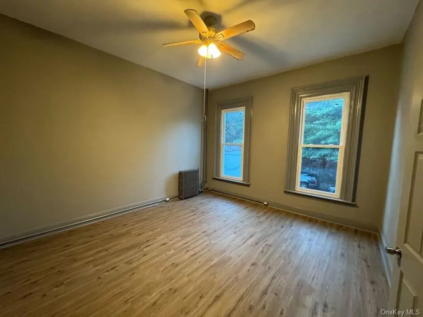 Unfurnished room with light wood-type flooring, a ceiling fan, and radiator heating unit Unfurnished room with light wood-type flooring, a ceiling fan, and radiator heating unit