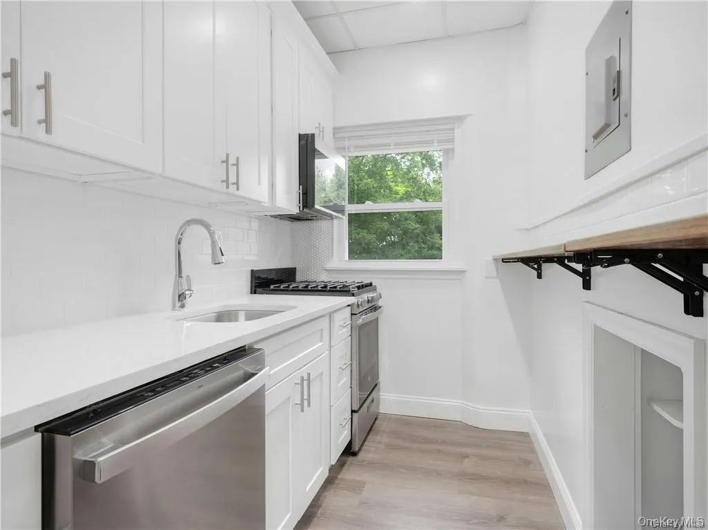 Kitchen featuring white cabinetry, appliances with stainless steel finishes, tasteful backsplash, light wood-style floors, and light stone countertops Kitchen featuring white cabinetry, appliances with stainless steel finishes, tasteful backsplash, light wood-style floors, and light stone countertops
