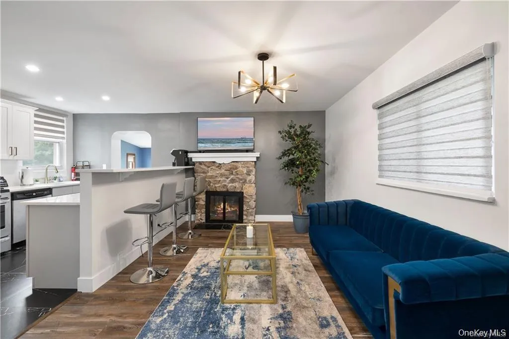 Living area featuring dark wood-style flooring, a stone fireplace, recessed lighting, and a chandelier Living area featuring dark wood-style flooring, a stone fireplace, recessed lighting, and a chandelier