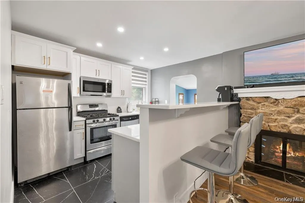 Kitchen featuring a kitchen bar, appliances with stainless steel finishes, white cabinets, recessed lighting, and dark marble finish floors Kitchen featuring a kitchen bar, appliances with stainless steel finishes, white cabinets, recessed lighting, and dark marble finish floors
