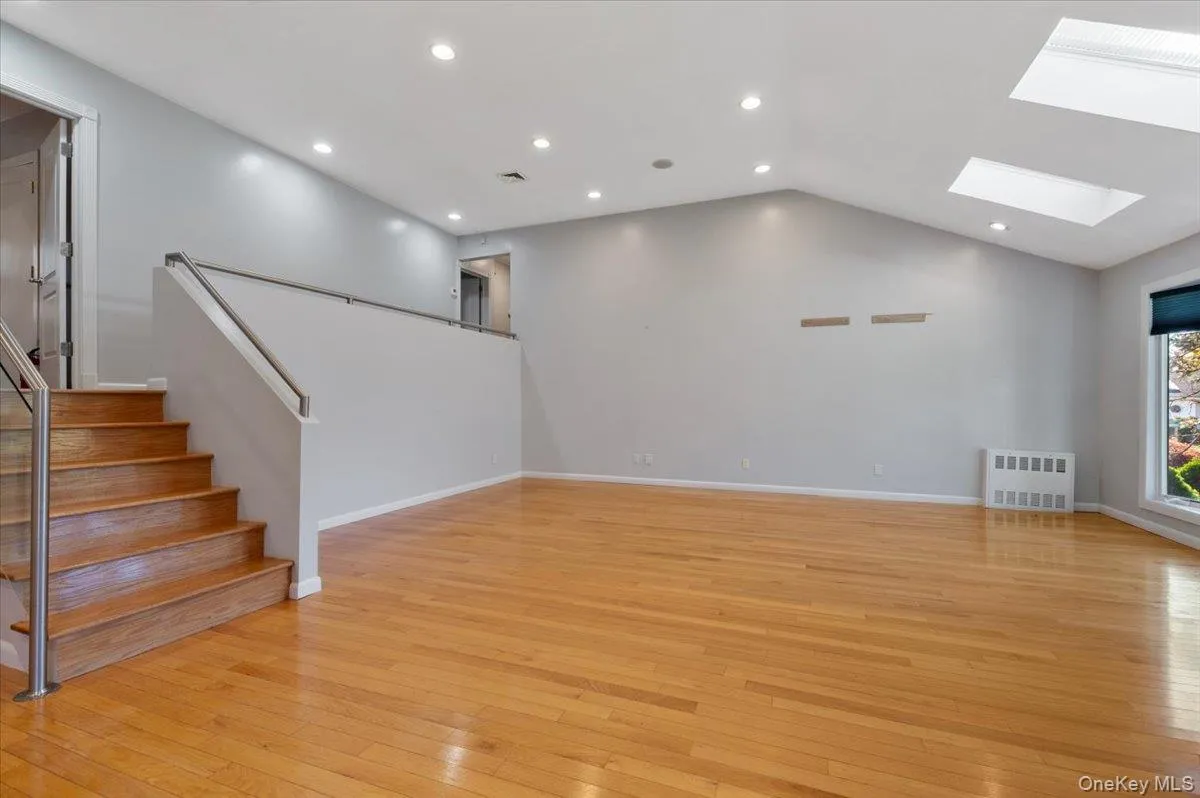 Unfurnished living room with stairway, light wood-style flooring, lofted ceiling, a skylight, and recessed lighting Unfurnished living room with stairway, light wood-style flooring, lofted ceiling, a skylight, and recessed lighting