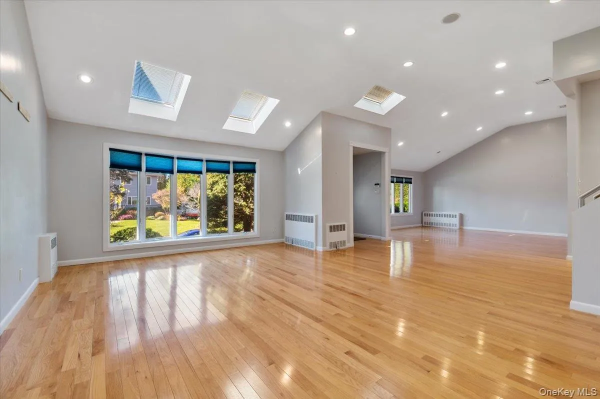 Unfurnished living room with light wood finished floors, radiator heating unit, recessed lighting, vaulted ceiling, and a skylight Unfurnished living room with light wood finished floors, radiator heating unit, recessed lighting, vaulted ceiling, and a skylight