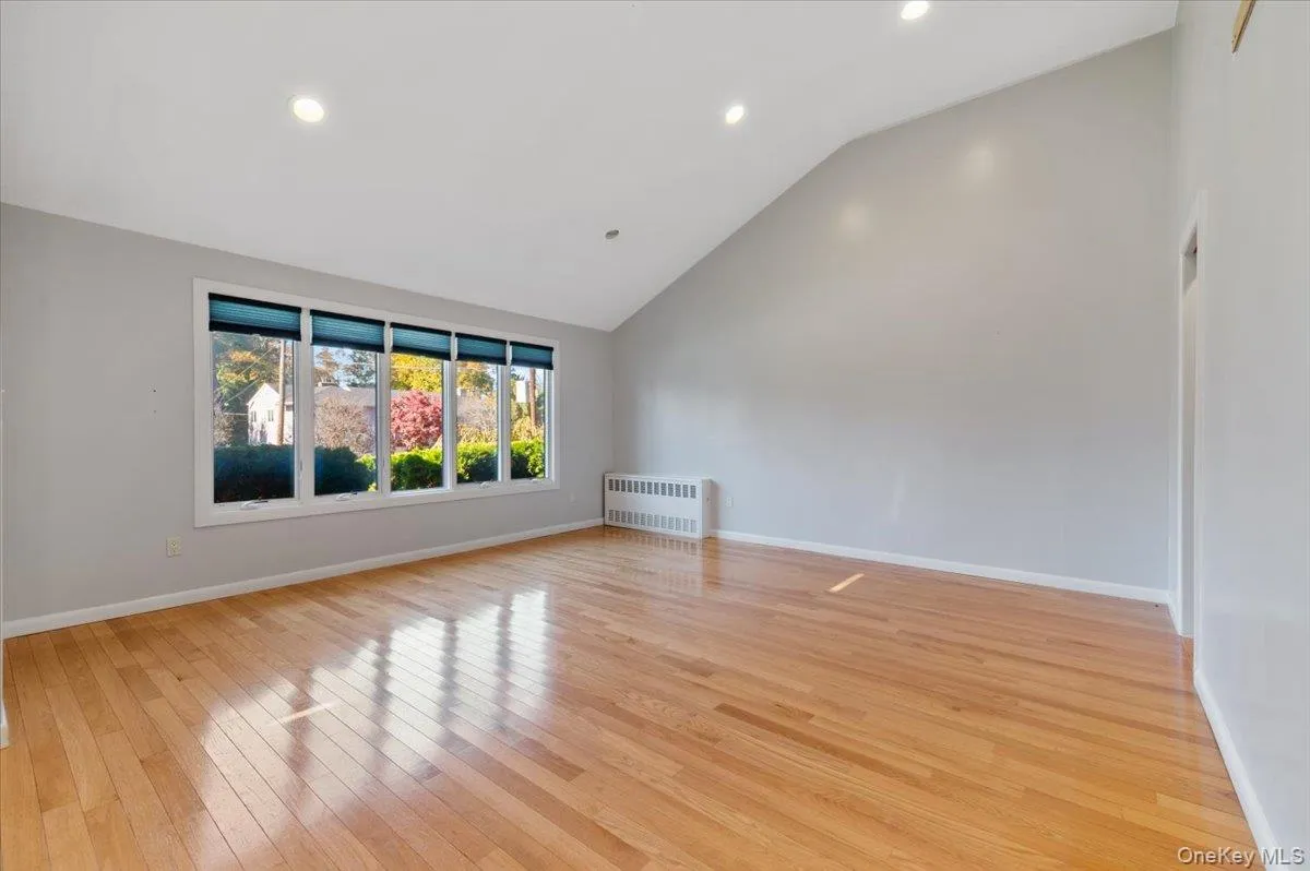 Unfurnished room featuring recessed lighting, radiator, high vaulted ceiling, and light wood-type flooring Unfurnished room featuring recessed lighting, radiator, high vaulted ceiling, and light wood-type flooring