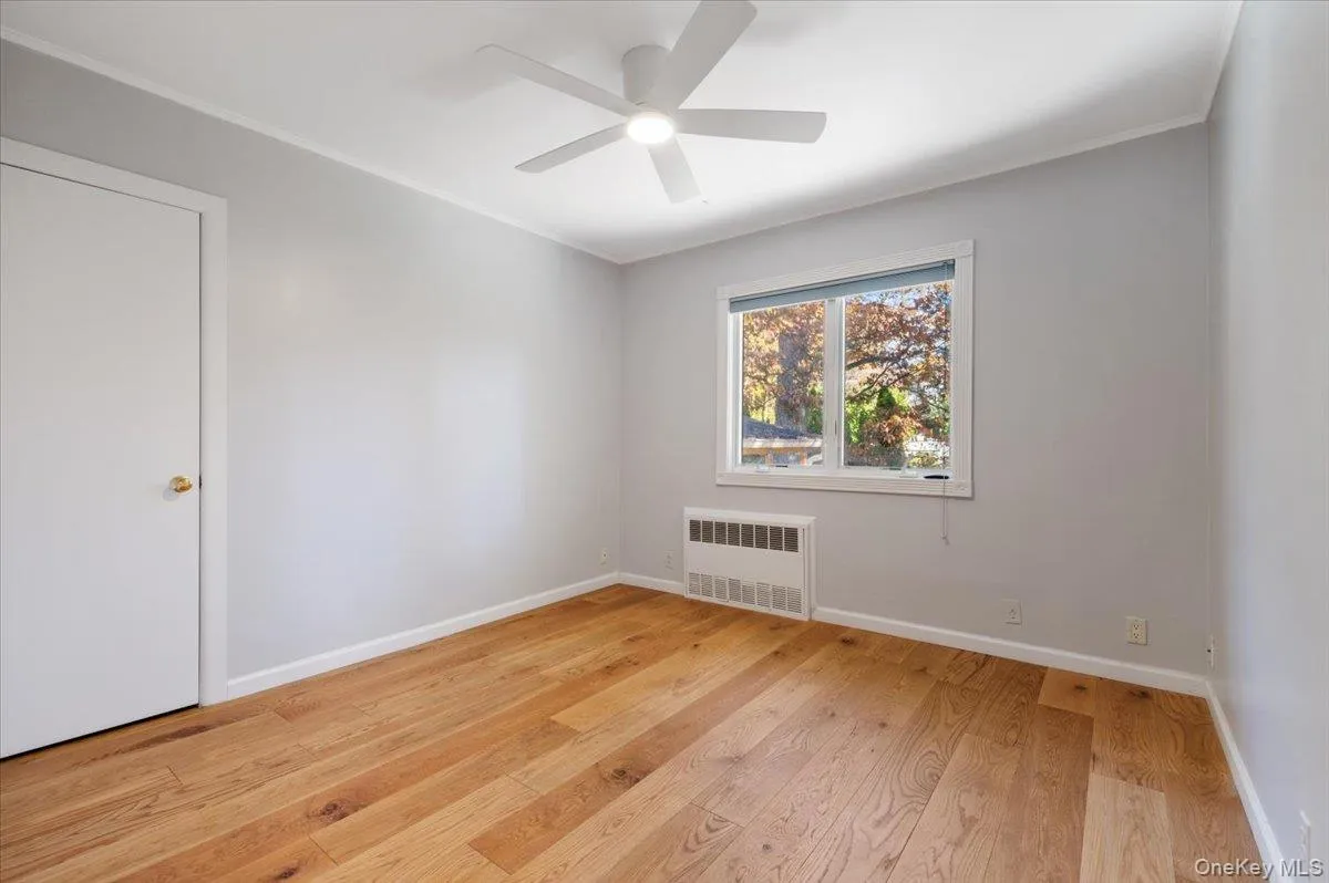 Spare room with light wood-style floors, crown molding, radiator, and a ceiling fan Spare room with light wood-style floors, crown molding, radiator, and a ceiling fan