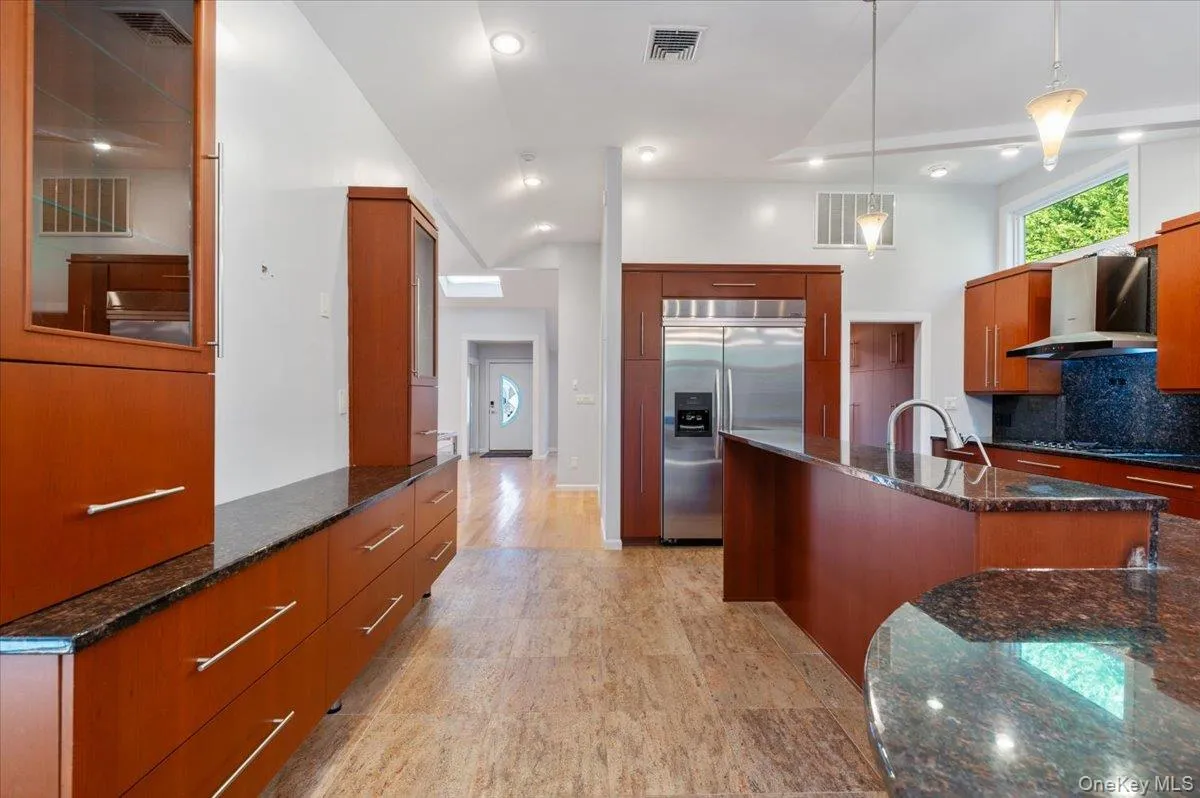 Kitchen featuring dark stone counters, stainless steel built in fridge, decorative light fixtures, wall chimney exhaust hood, and decorative backsplash Kitchen featuring dark stone counters, stainless steel built in fridge, decorative light fixtures, wall chimney exhaust hood, and decorative backsplash