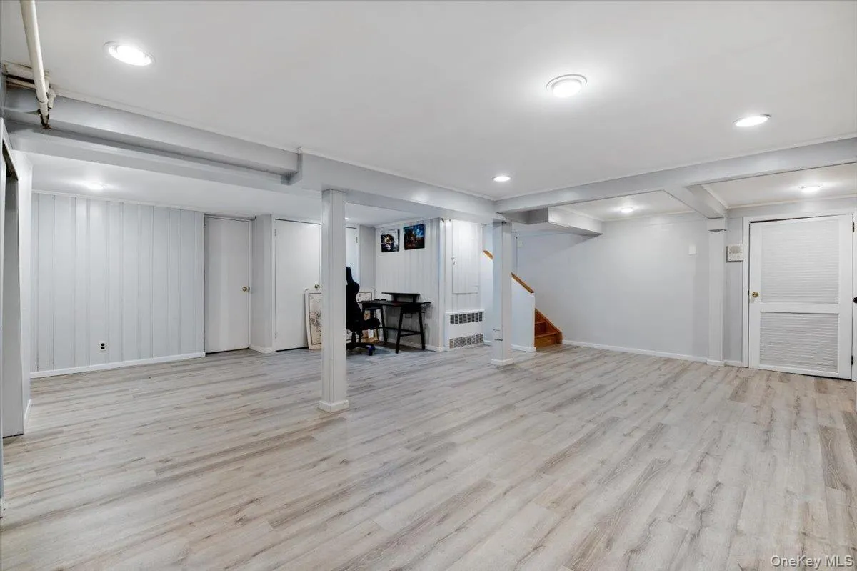 Finished basement with light wood finished floors, an office area, radiator heating unit, recessed lighting, and stairs Finished basement with light wood finished floors, an office area, radiator heating unit, recessed lighting, and stairs