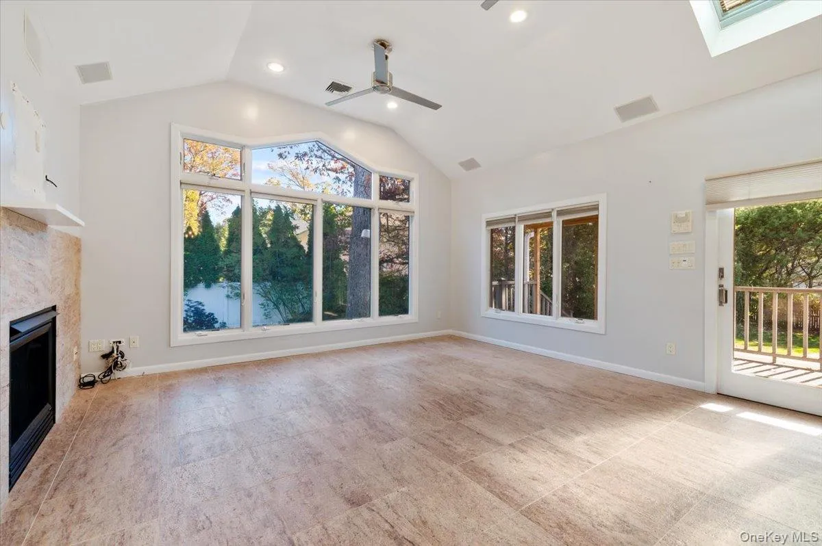Unfurnished living room featuring healthy amount of natural light, vaulted ceiling, a fireplace, ceiling fan, and a skylight Unfurnished living room featuring healthy amount of natural light, vaulted ceiling, a fireplace, ceiling fan, and a skylight