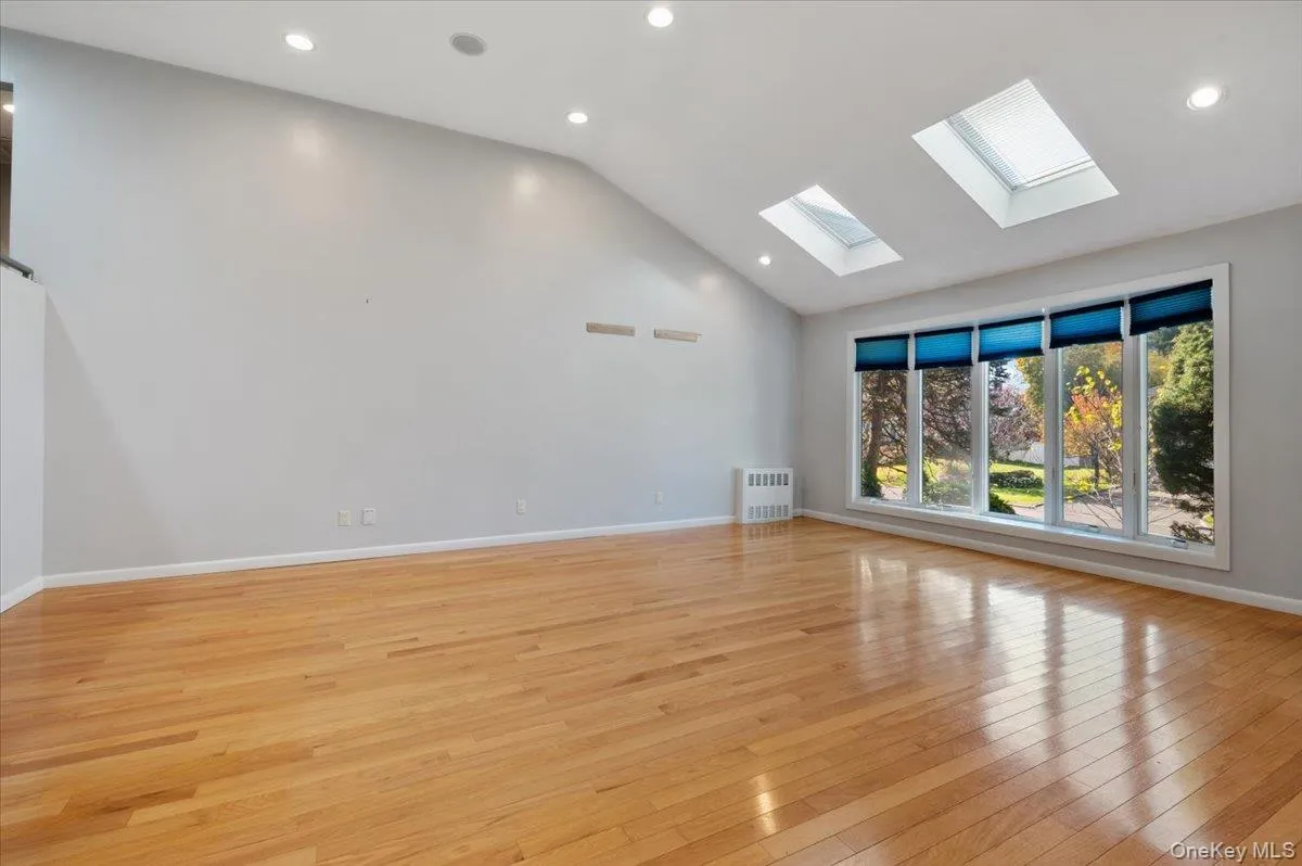 Unfurnished room with light wood-style floors, recessed lighting, high vaulted ceiling, a skylight, and radiator heating unit Unfurnished room with light wood-style floors, recessed lighting, high vaulted ceiling, a skylight, and radiator heating unit