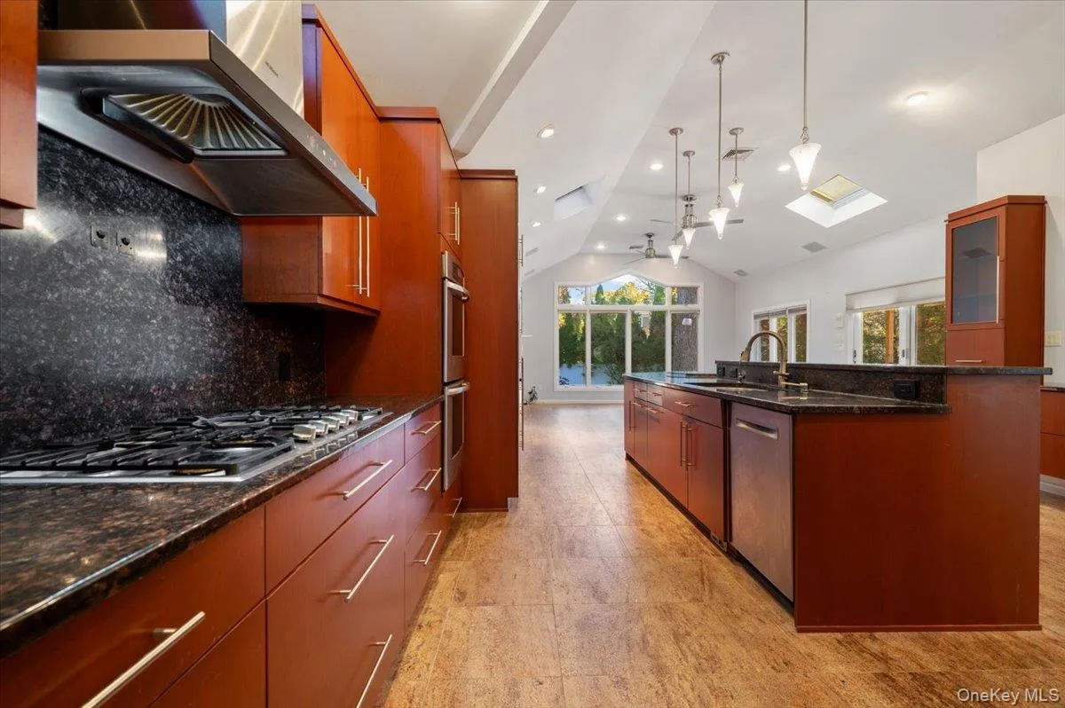 Kitchen featuring dark stone counters, wall chimney range hood, lofted ceiling, decorative backsplash, and pendant lighting Kitchen featuring dark stone counters, wall chimney range hood, lofted ceiling, decorative backsplash, and pendant lighting