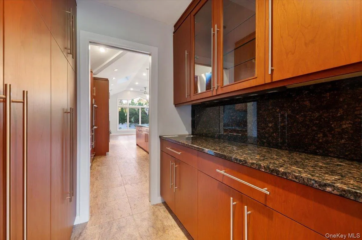 Bar with glass insert cabinets, brown cabinetry, dark stone counters, and vaulted ceiling Bar with glass insert cabinets, brown cabinetry, dark stone counters, and vaulted ceiling