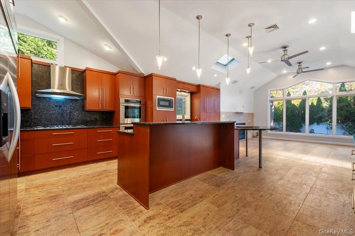 Kitchen with backsplash, a skylight, hanging light fixtures, wall chimney range hood, and a kitchen breakfast bar Kitchen with backsplash, a skylight, hanging light fixtures, wall chimney range hood, and a kitchen breakfast bar