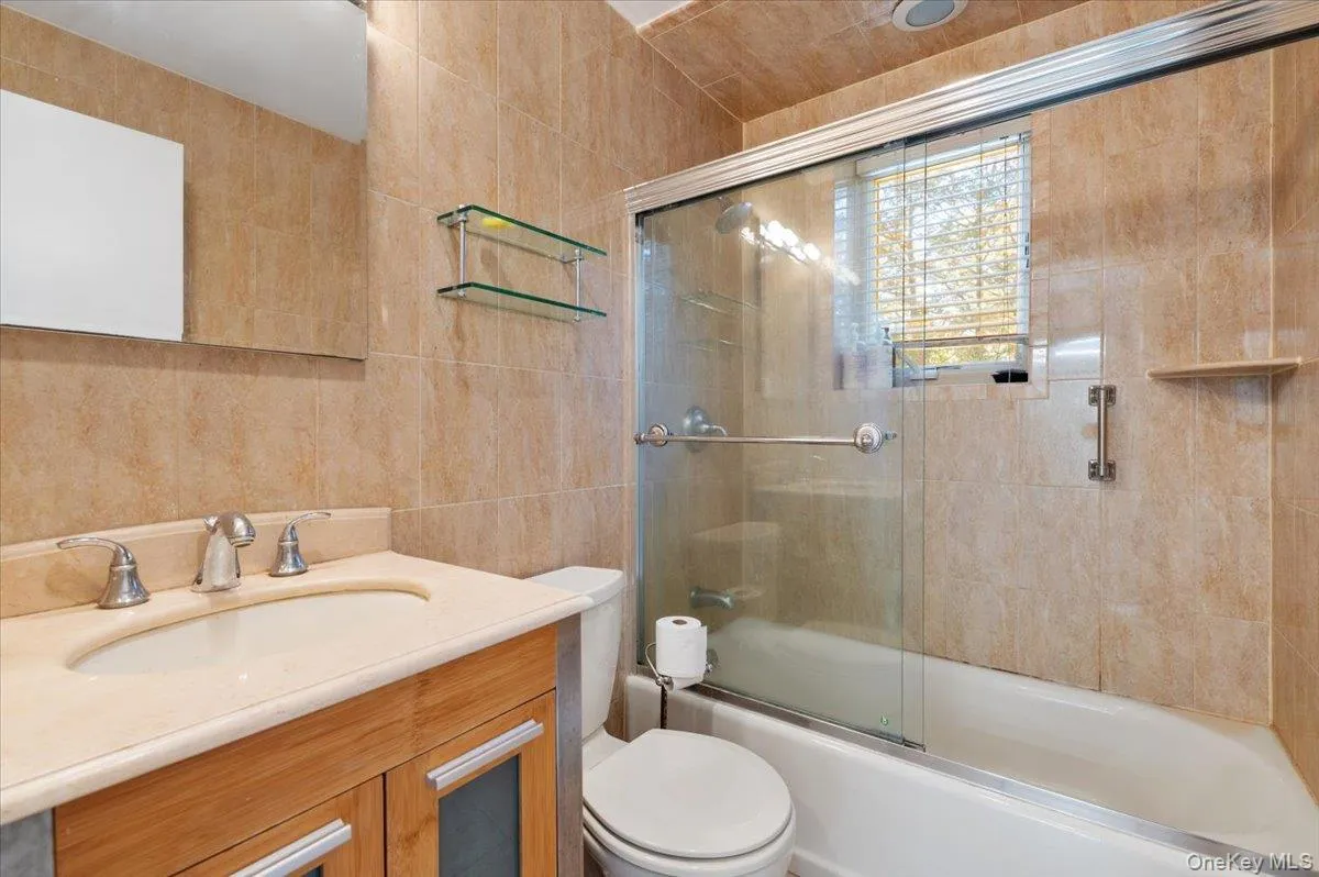 Full bathroom featuring tile walls, vanity, and bath / shower combo with glass door Full bathroom featuring tile walls, vanity, and bath / shower combo with glass door