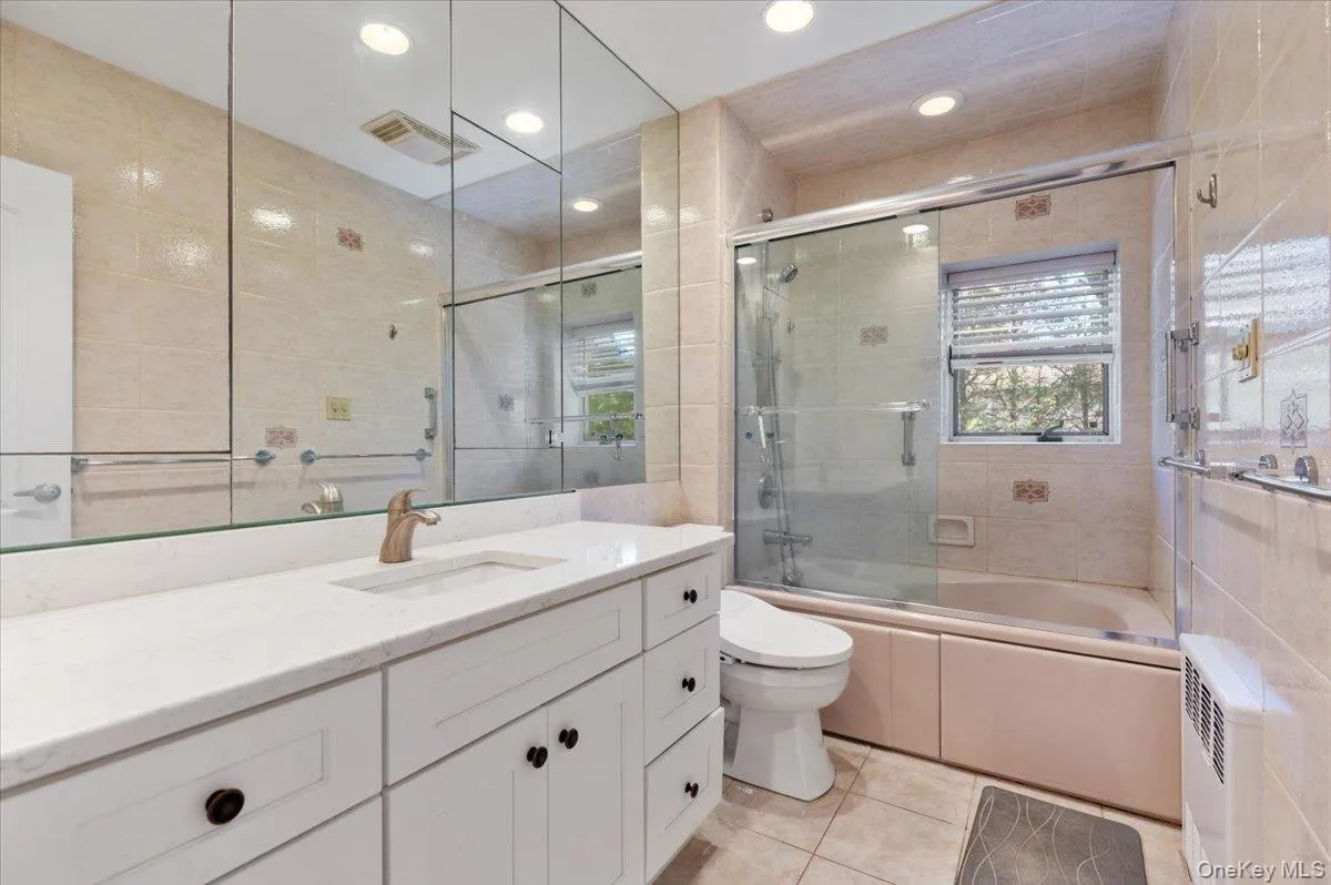 Bathroom with vanity, enclosed tub / shower combo, tile walls, light tile patterned floors, and recessed lighting Bathroom with vanity, enclosed tub / shower combo, tile walls, light tile patterned floors, and recessed lighting