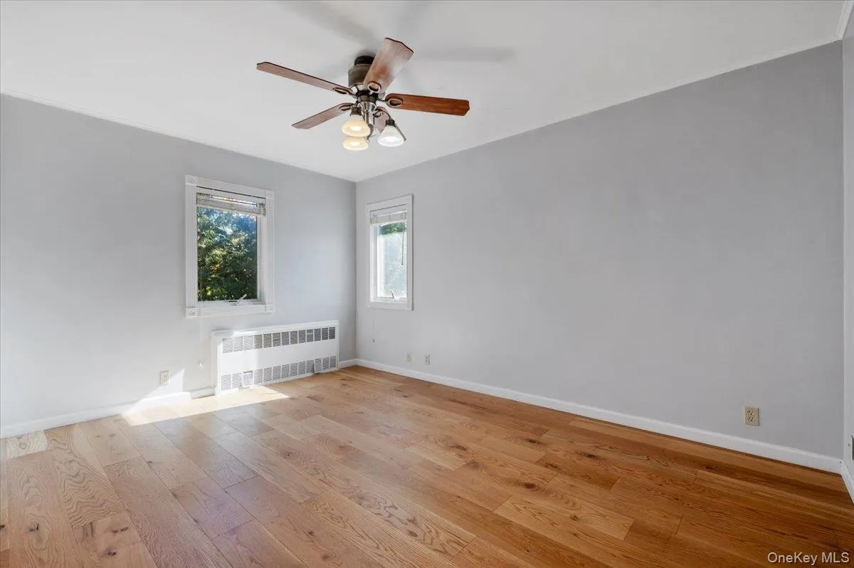 Unfurnished room with radiator heating unit, light wood-style floors, and ceiling fan Unfurnished room with radiator heating unit, light wood-style floors, and ceiling fan