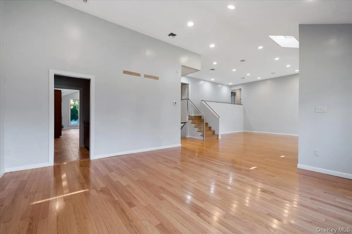 Unfurnished living room with light wood-type flooring, recessed lighting, a skylight, and stairway Unfurnished living room with light wood-type flooring, recessed lighting, a skylight, and stairway
