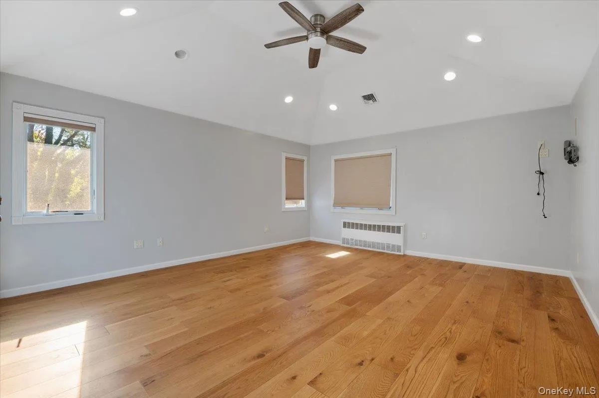 Empty room with light wood-type flooring, radiator heating unit, recessed lighting, ceiling fan, and vaulted ceiling Empty room with light wood-type flooring, radiator heating unit, recessed lighting, ceiling fan, and vaulted ceiling