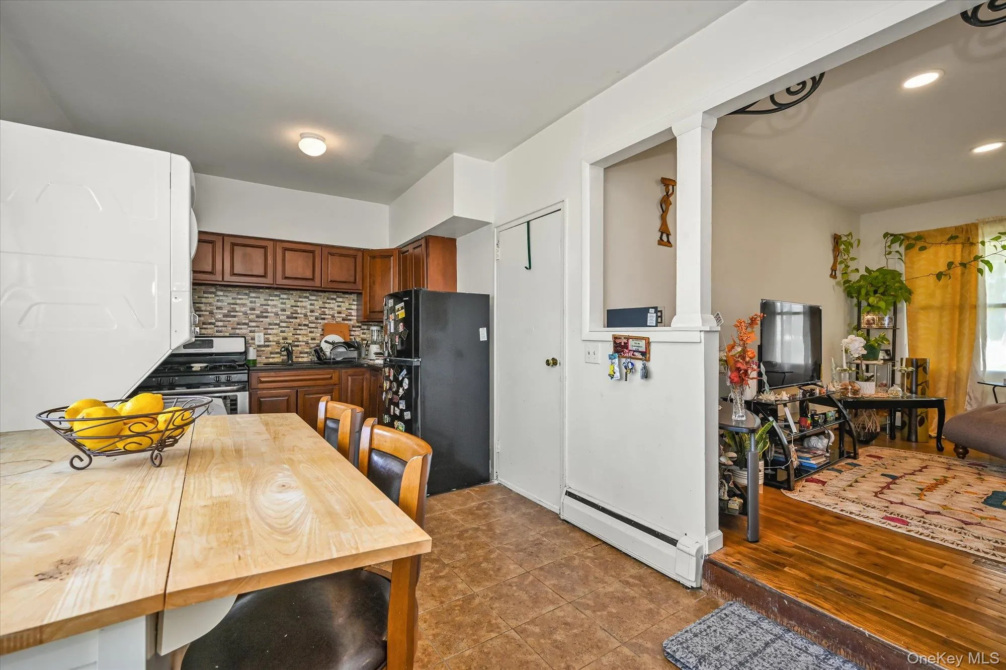 Kitchen featuring baseboard heating, freestanding refrigerator, backsplash, dark countertops, and brown cabinets Kitchen featuring baseboard heating, freestanding refrigerator, backsplash, dark countertops, and brown cabinets