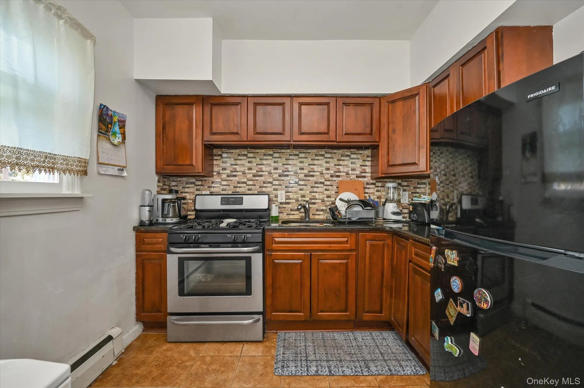 Kitchen with gas range, freestanding refrigerator, tasteful backsplash, a baseboard radiator, and dark stone countertops Kitchen with gas range, freestanding refrigerator, tasteful backsplash, a baseboard radiator, and dark stone countertops