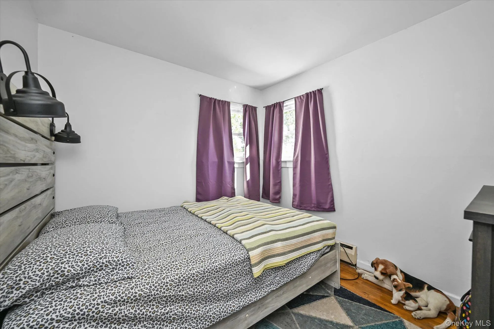 Bedroom featuring wood finished floors and a baseboard heating unit Bedroom featuring wood finished floors and a baseboard heating unit