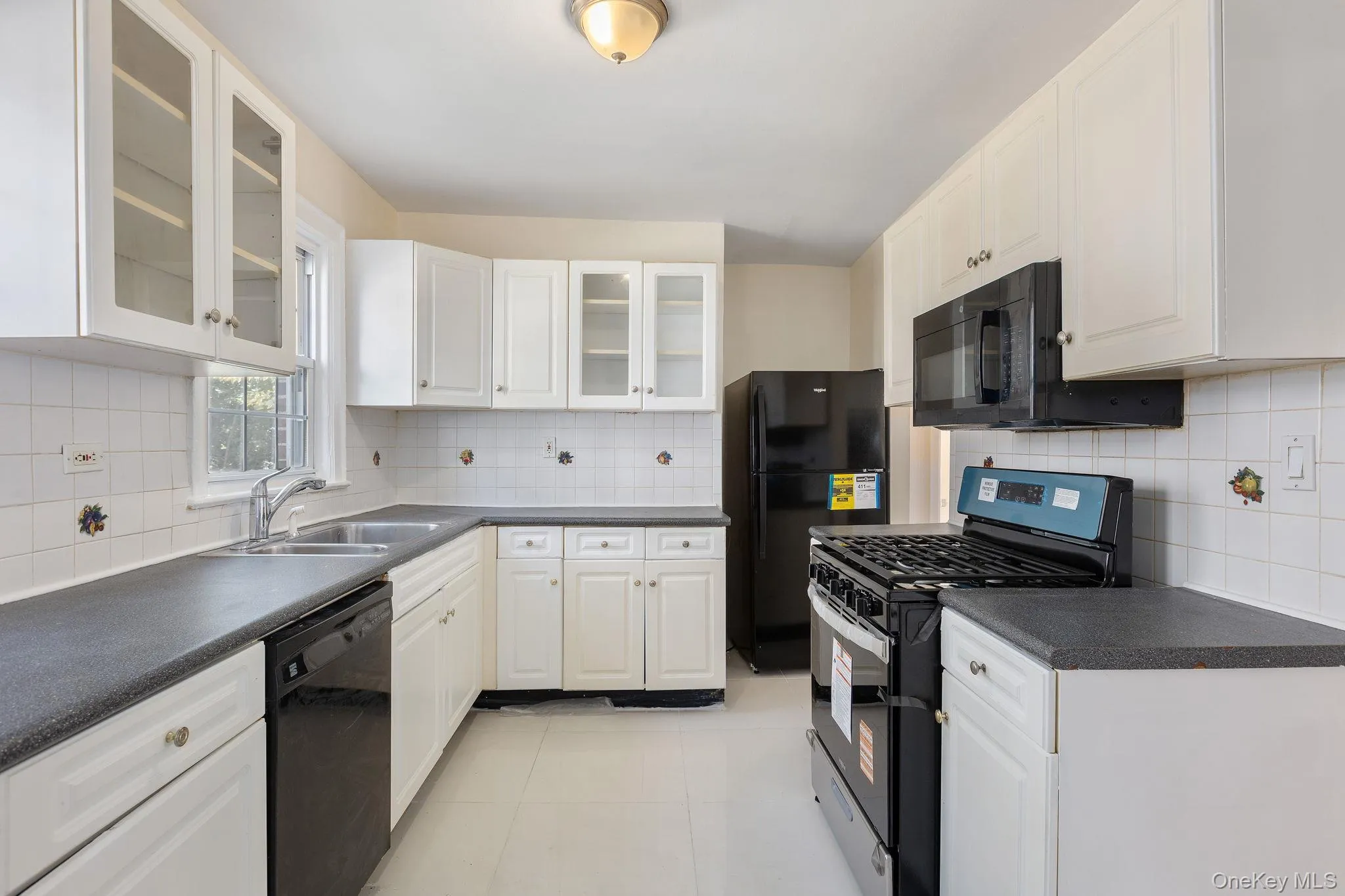 Kitchen featuring black appliances, glass insert cabinets, dark countertops, decorative backsplash, and white cabinetry Kitchen featuring black appliances, glass insert cabinets, dark countertops, decorative backsplash, and white cabinetry