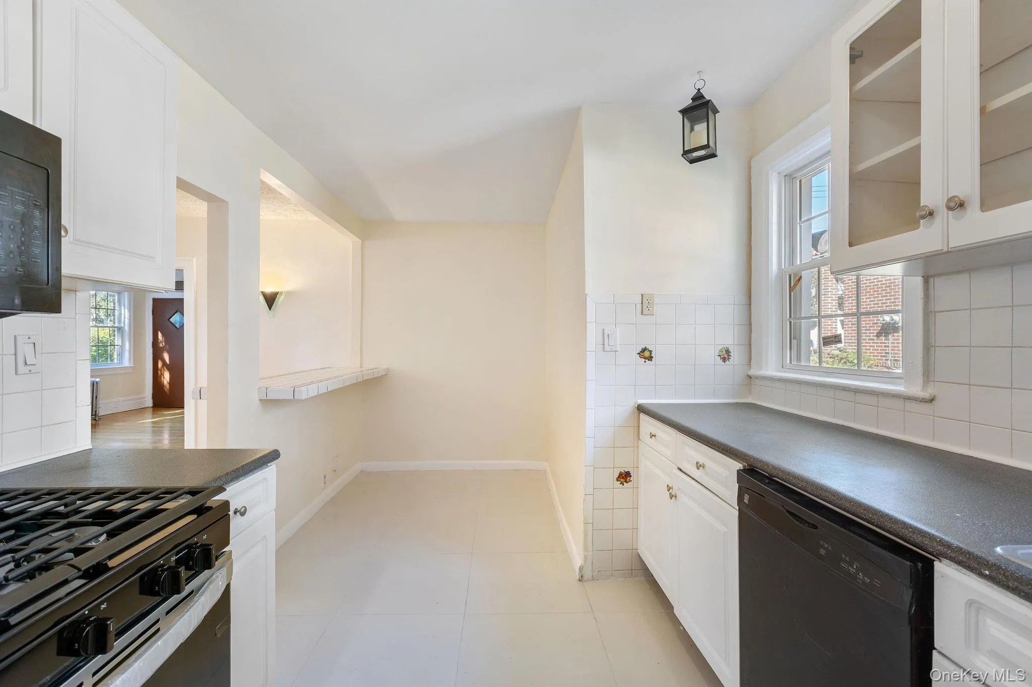 Kitchen featuring white cabinetry, dark countertops, black appliances, decorative backsplash, and tile walls Kitchen featuring white cabinetry, dark countertops, black appliances, decorative backsplash, and tile walls